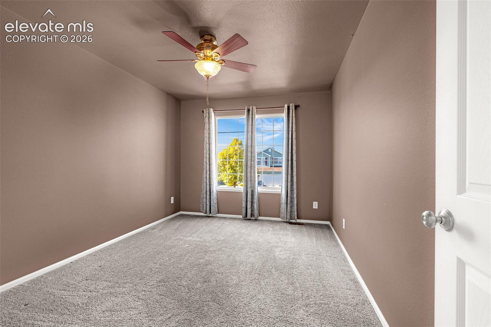 Interior room featuring wall-to-wall carpeting, a central ceiling fan with integrated lighting, and dual-pane windows with muntin bars
