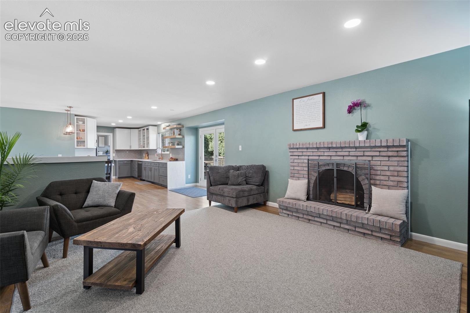 Brick fireplace featuring a raised hearth, recessed lighting, double glass doors with paneled trim, and built-in kitchen cabinetry with stone-finish countertops