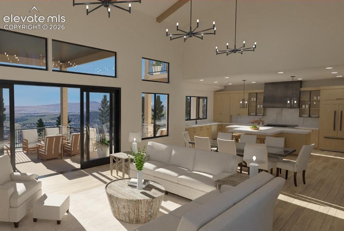 Vaulted ceilings featuring exposed beams and modern chandeliers, a kitchen with light wood-finish cabinetry, a large kitchen island with seating, a sliding glass door opening to an outdoor deck, and wood-finish flooring