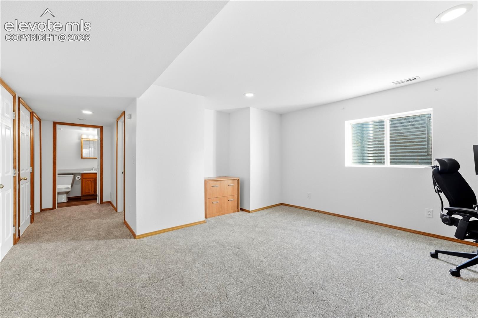 Spacious room featuring light-colored carpeting, white walls, recessed lighting, and window wells