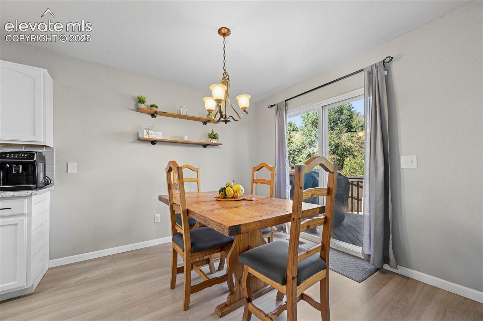 Dining area featuring LVP flooring, two wall-mounted industrial-style floating shelves, a multi-light metal chandelier, and a sliding glass door