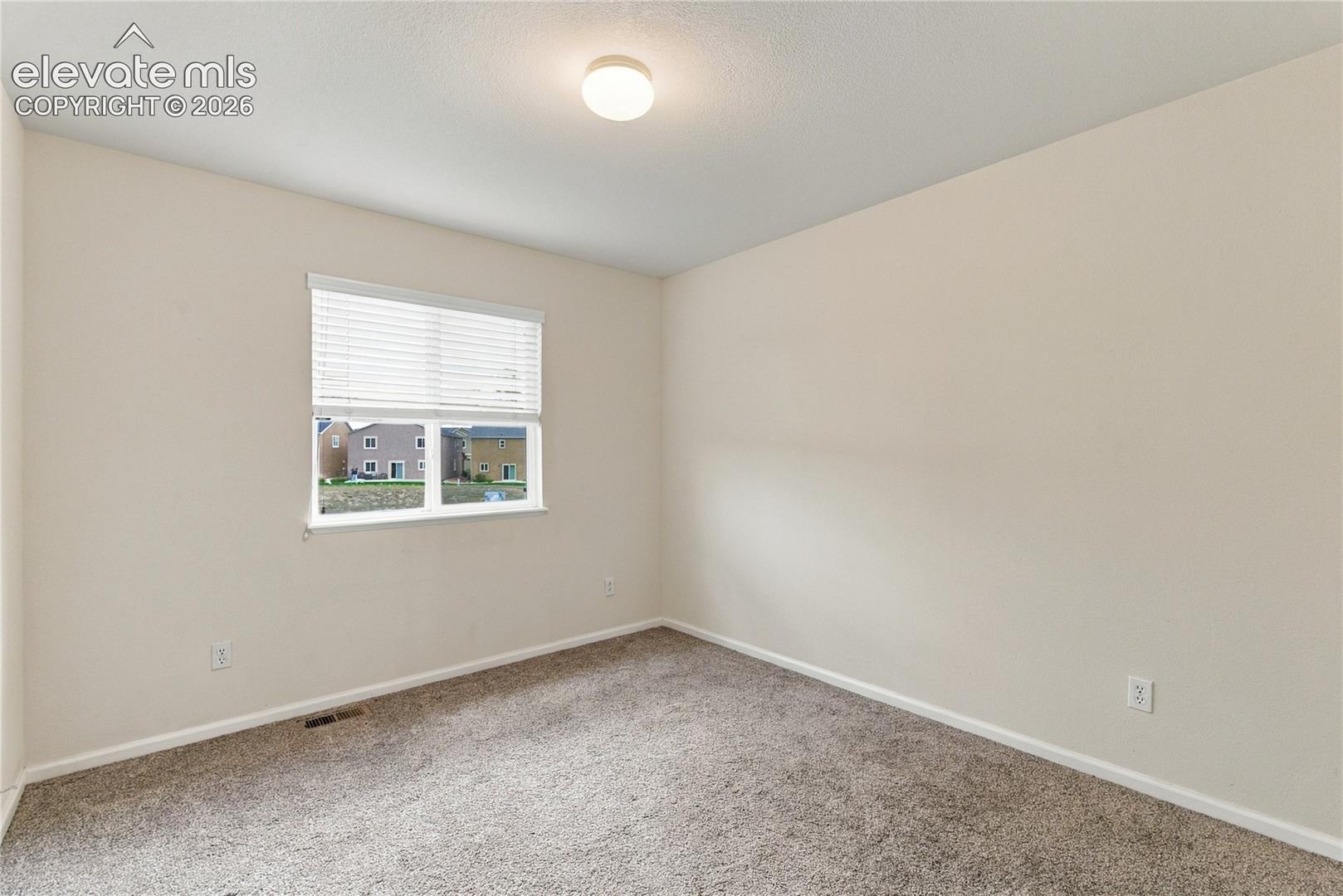 Neutral-toned interior space featuring carpeting, a single-pane window with horizontal blinds, and a flush-mount ceiling light fixture
