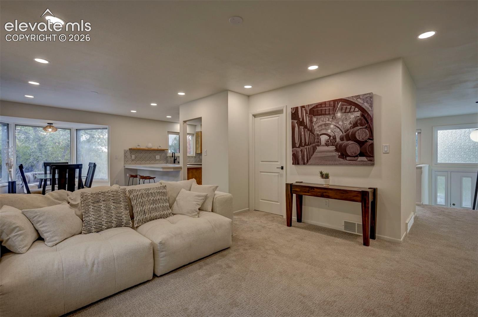 Neutral-toned carpet, recessed lighting, multi-panel interior door, and textured tile kitchen backsplash