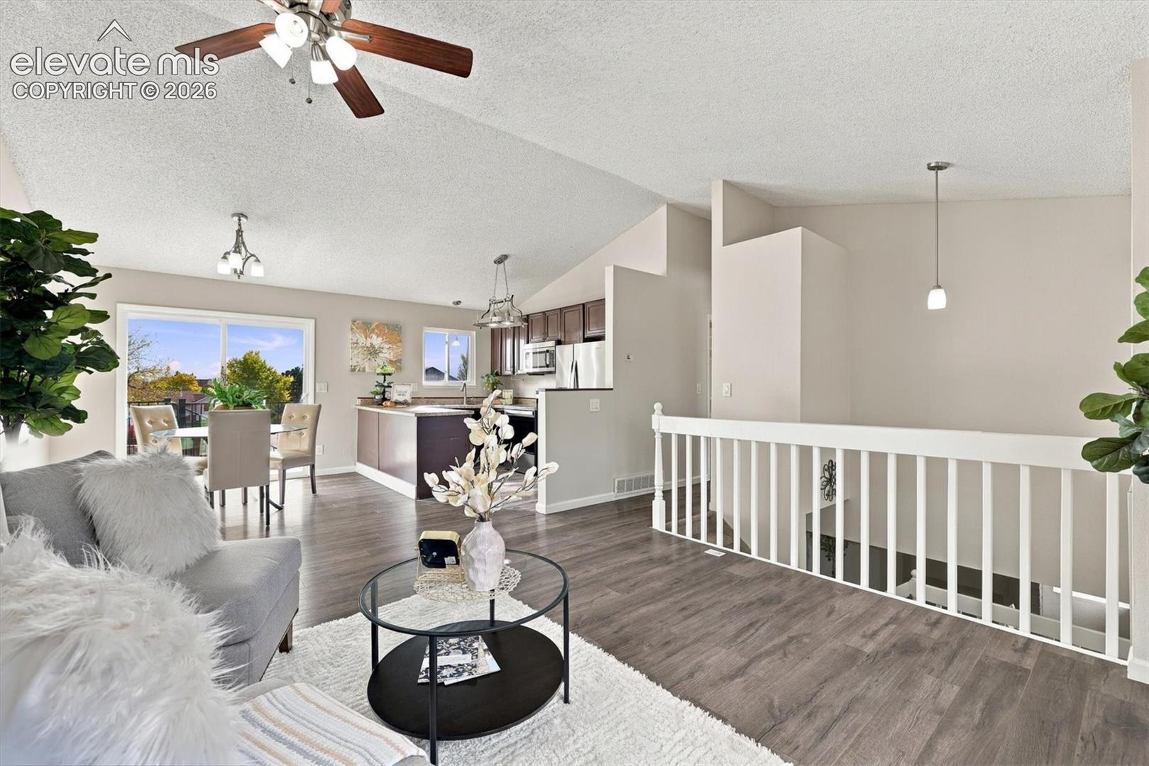 Vaulted ceilings, wood-finish flooring, white spindle staircase railing, and multiple pendant light fixtures