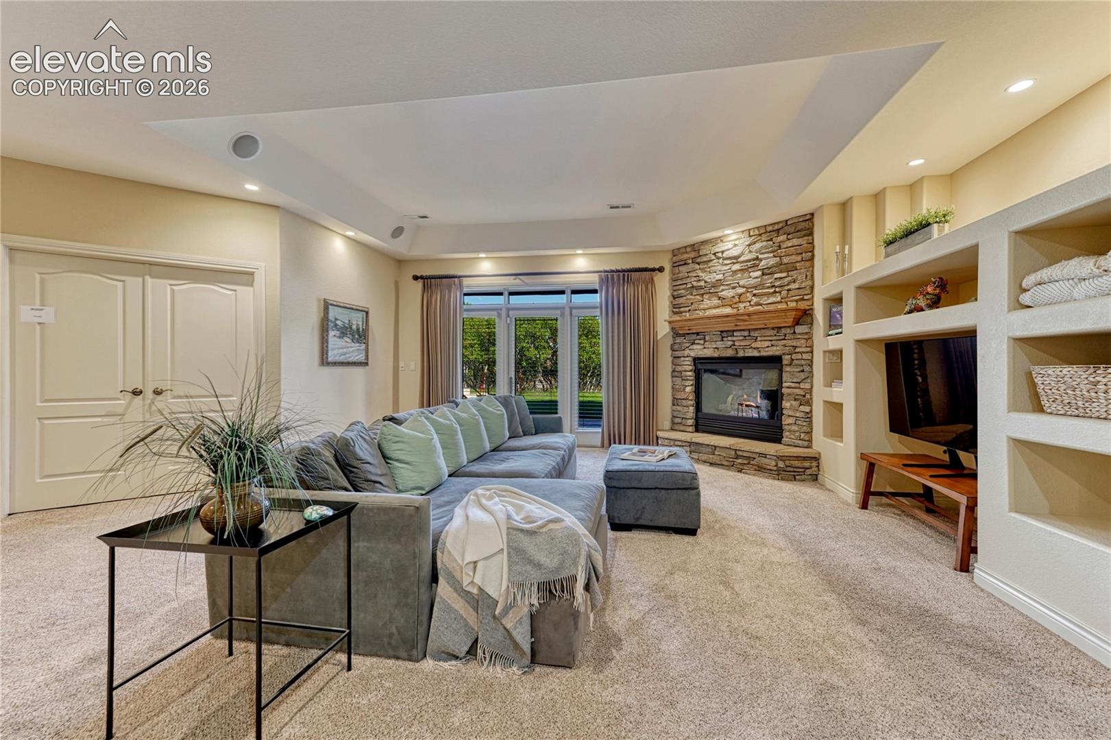 Corner stone-faced fireplace with wood mantel, built-in shelving, recessed lighting, and multi-panel glass door