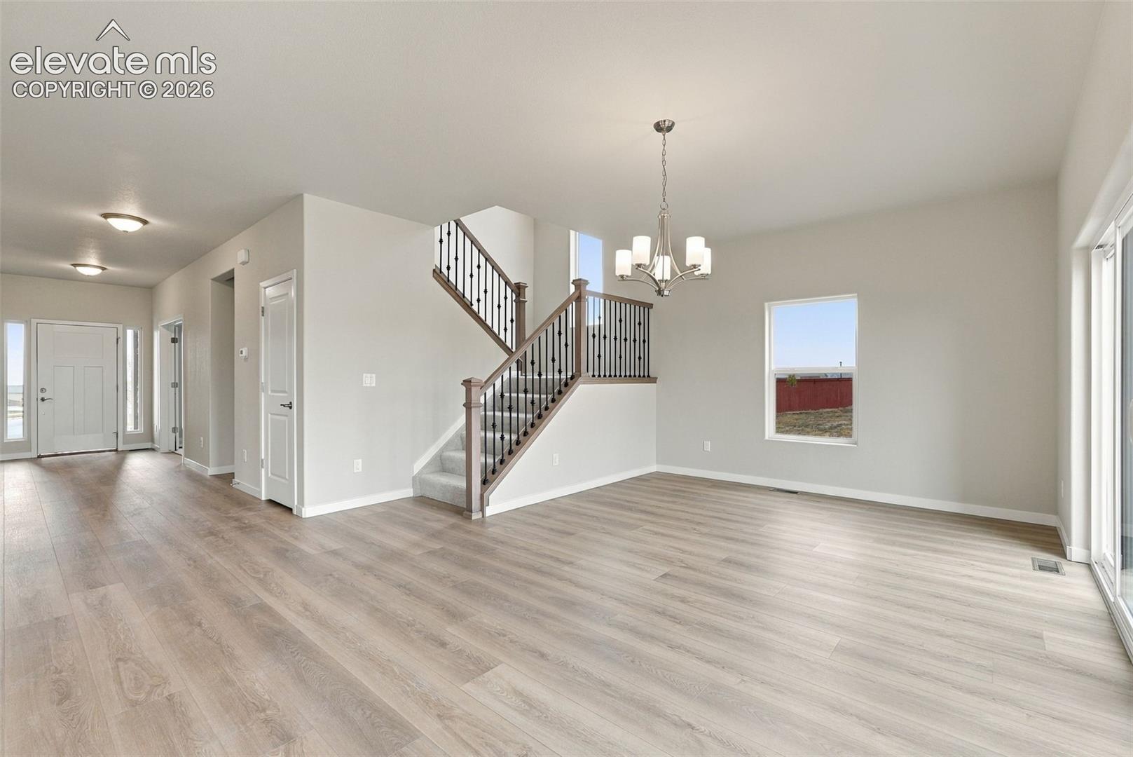Open interior featuring wood-finish flooring, staircase with metal balusters and wood handrail, multi-light chandelier, and sliding glass door