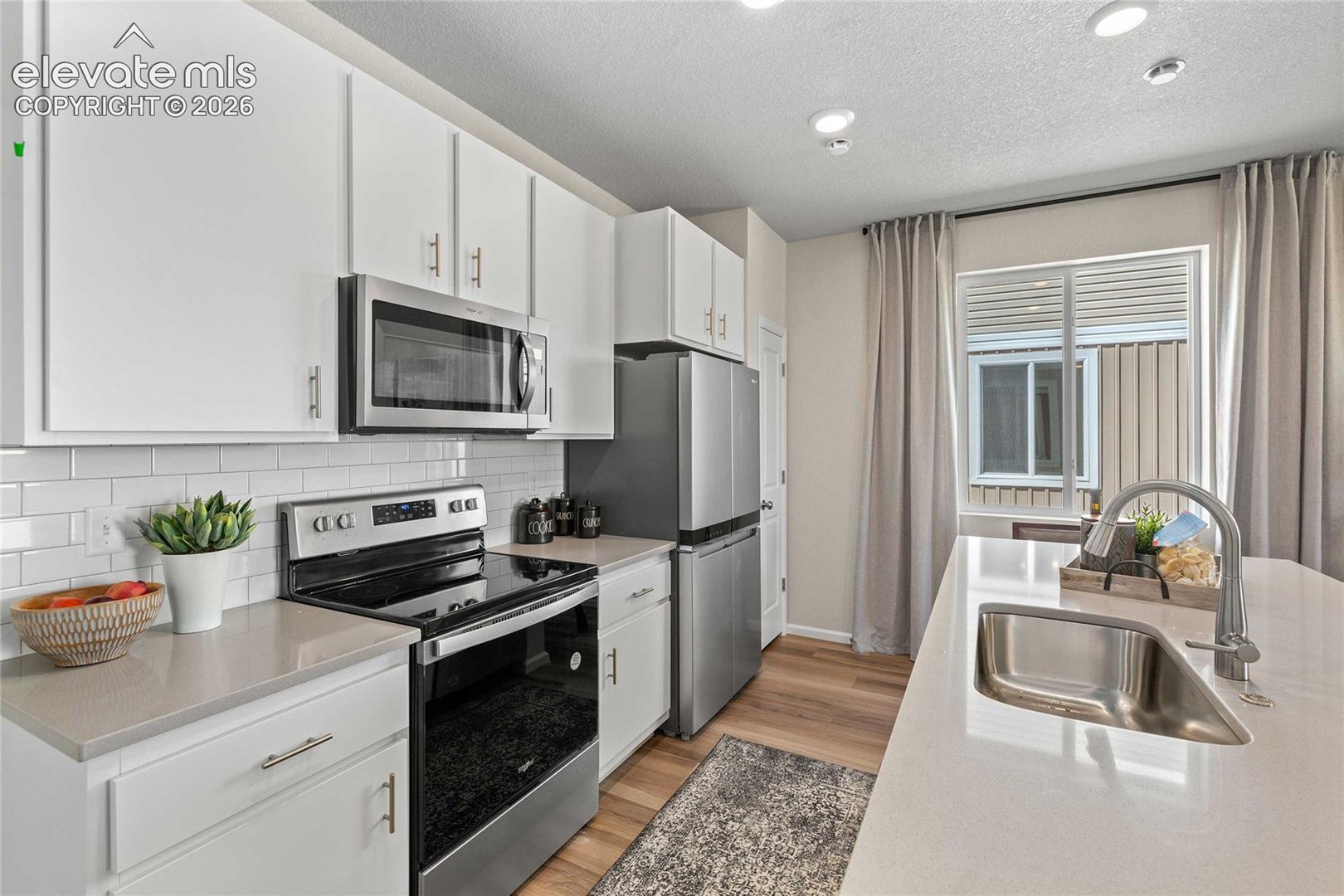 White cabinetry, stainless steel appliances, subway tile backsplash, light-toned countertops, and wood-finish flooring
*photos of a model home*