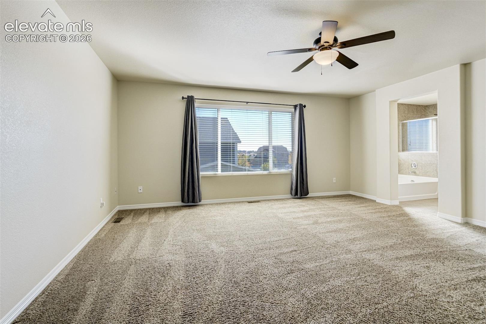 Spacious room with plush carpeting, ceiling fan, large window, and an arched doorway opening to a bathroom featuring a built-in tub
