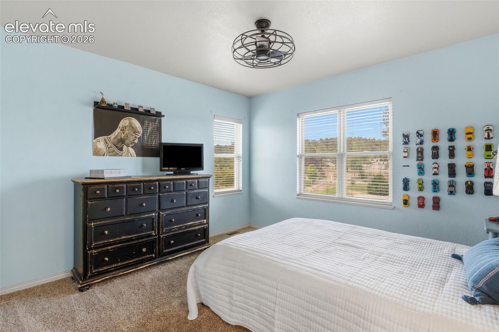 Bedroom featuring two windows with horizontal blinds, overhead ceiling fan with light fixture, light blue painted walls, and textured carpeting