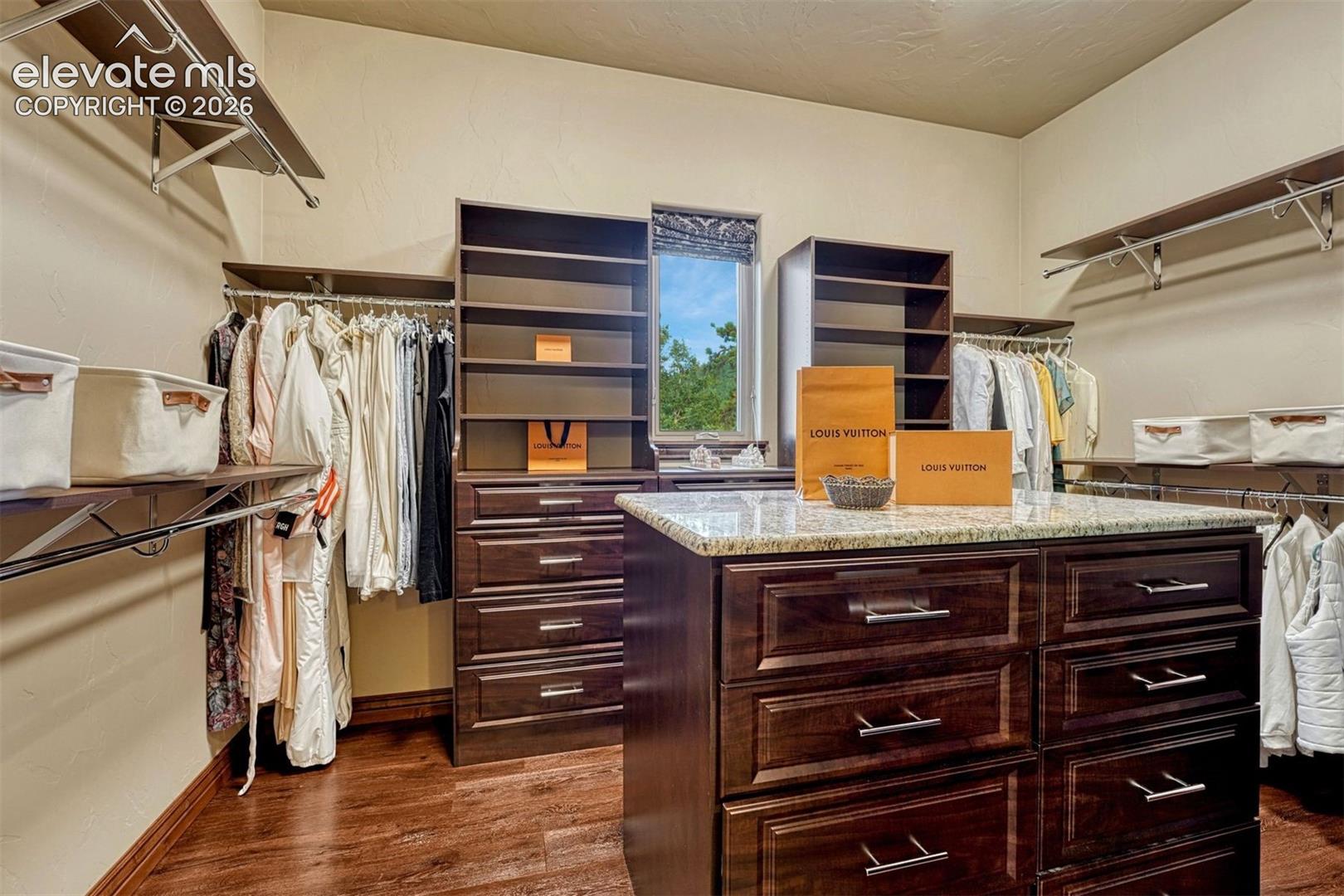 Custom closet organization system featuring wood-finish cabinetry, metal hanging rods, and an island with a stone-finish countertop