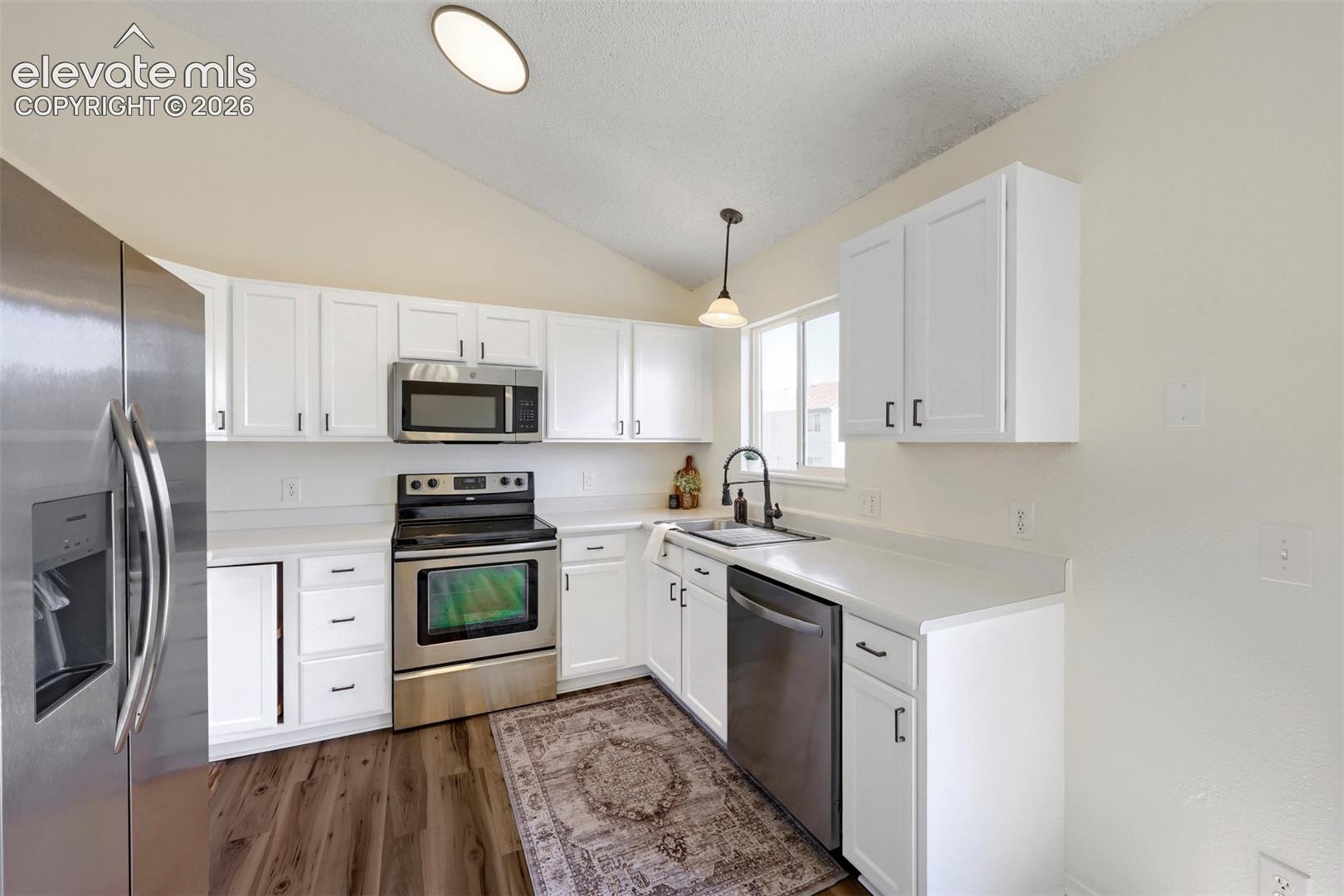 Kitchen featuring white cabinetry, stainless steel appliances, white countertops, wood-finish flooring, and a vaulted ceiling