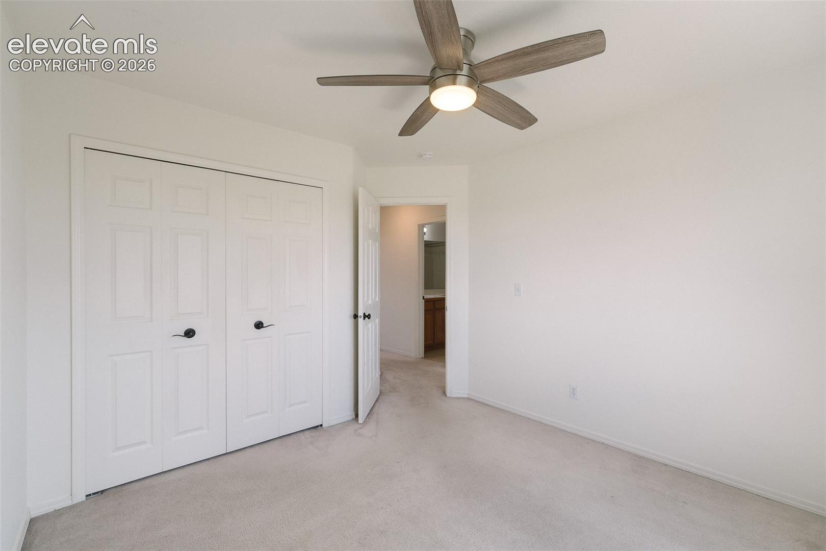 Ceiling fan with light fixture, light-colored carpet flooring, white paneled bifold closet doors, and white walls