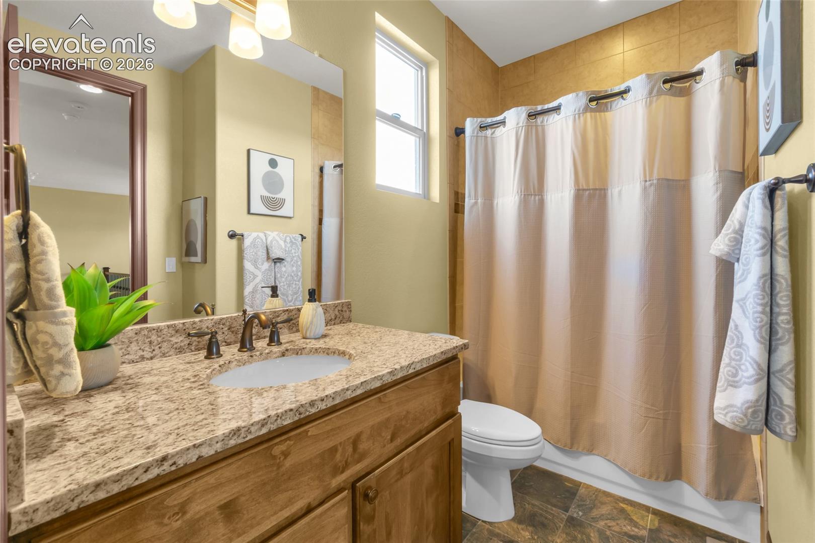 Bathroom featuring a wood vanity with a stone-finish countertop, undermount sink, multi-light fixture, and ceramic tile tub surround