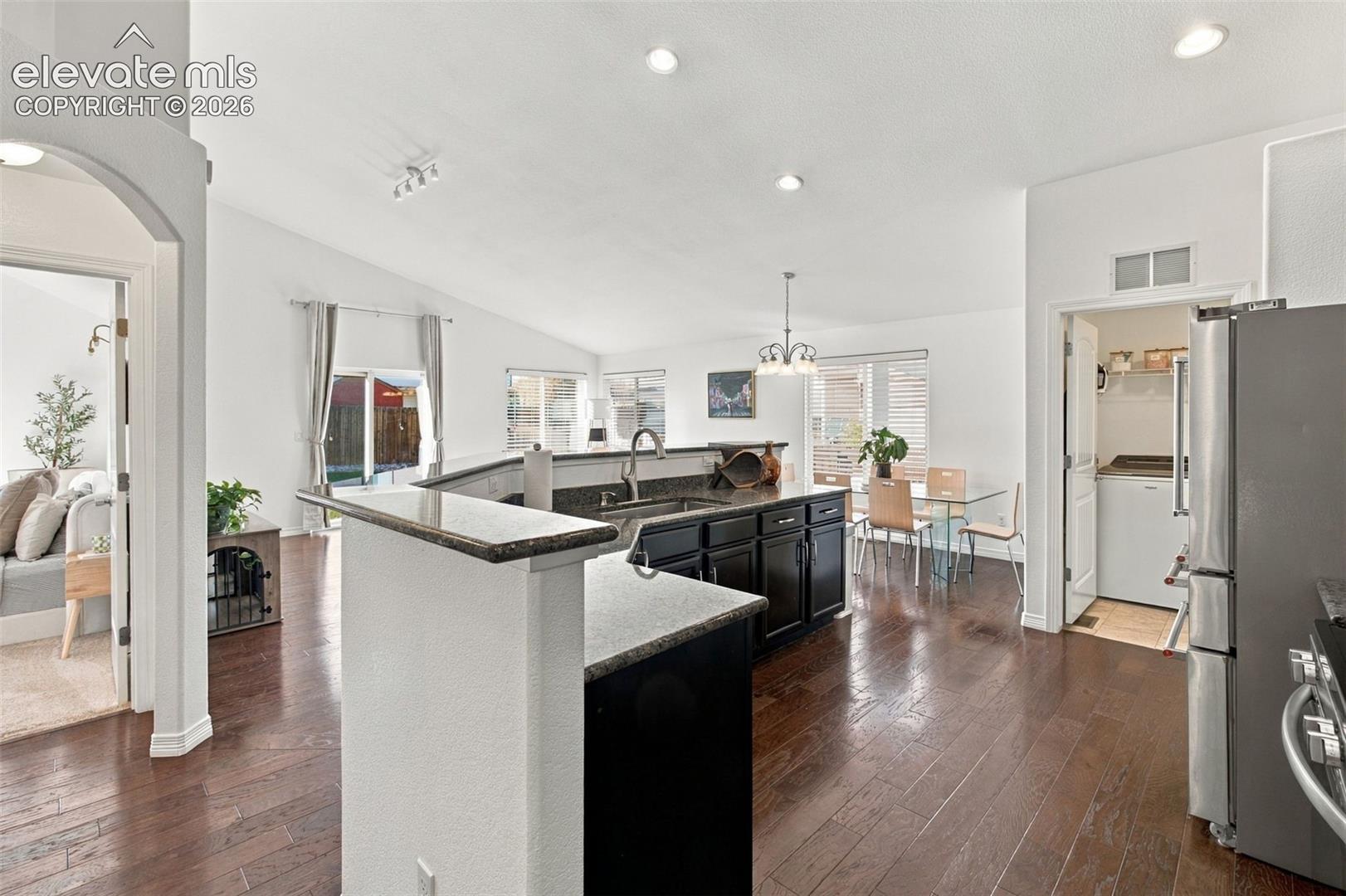 Open-concept kitchen and living area featuring high vaulted ceilings, dark wood-finish flooring, dark cabinetry with stone countertops, and recessed lighting
