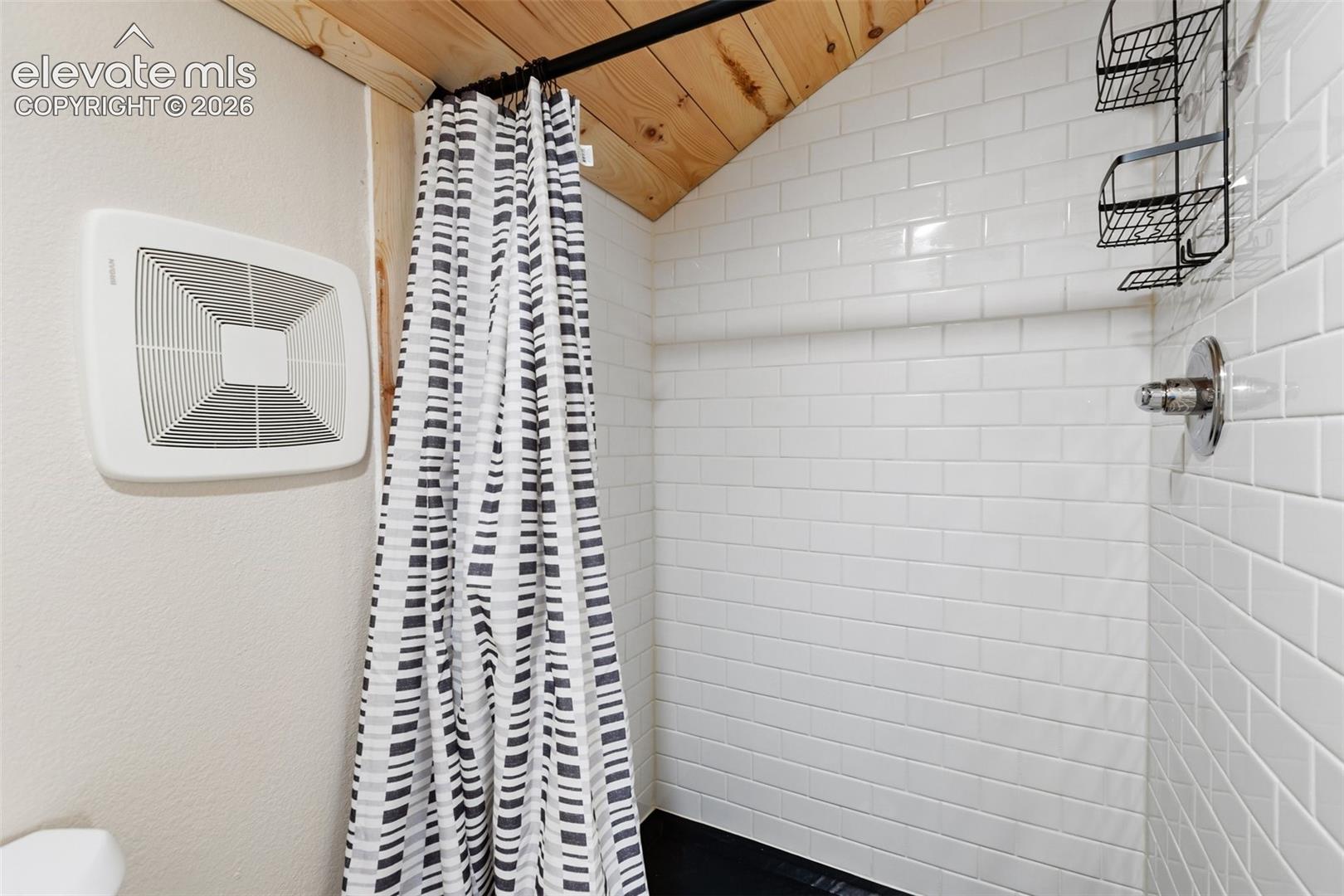 Shower enclosure featuring white subway tile walls, natural wood-plank ceiling, and a metallic shower fixture