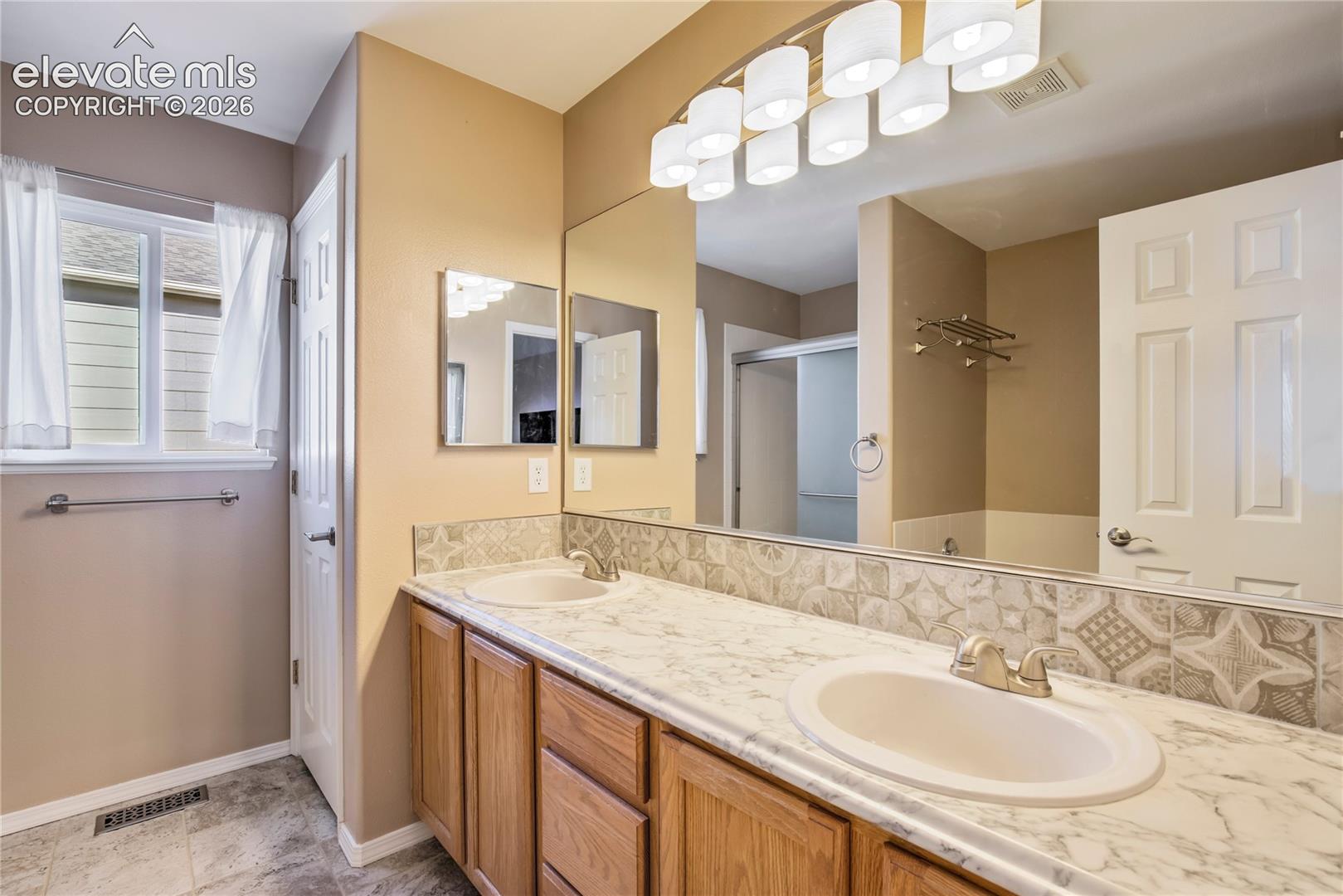 The adjoining 5-piece primary bath features an extended double vanity with generous counter space, abundant cabinetry + a window bringing in natural light.
