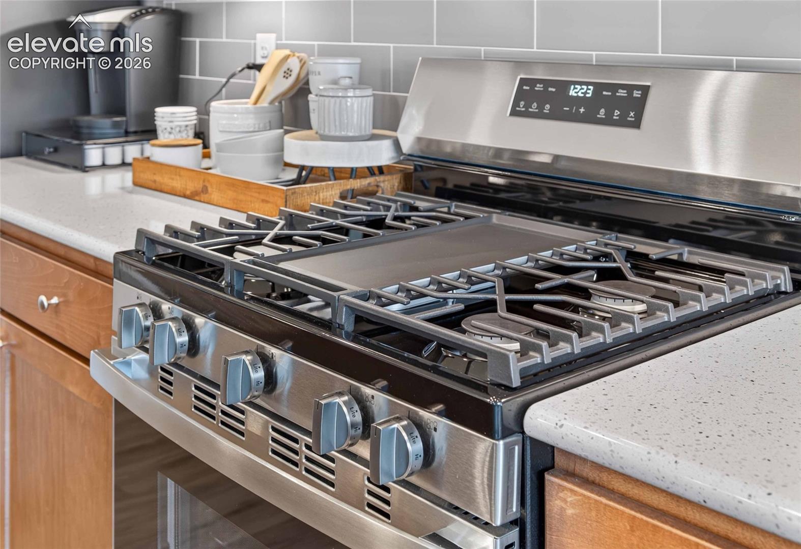 Stainless steel gas range with integrated center griddle, solid surface countertops, and grey subway tile backsplash