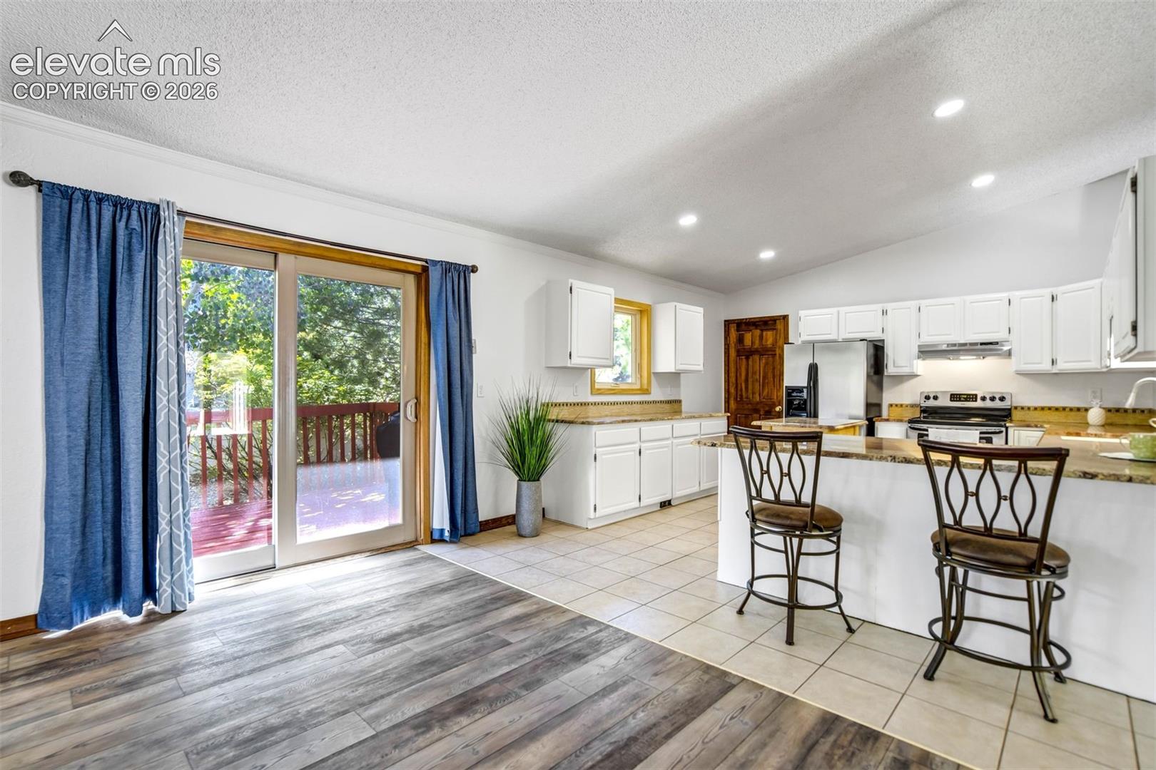 Open-concept kitchen and living area featuring wood-finish flooring, white cabinetry, a kitchen island with seating, a tile backsplash, and a sliding glass door leading to a deck