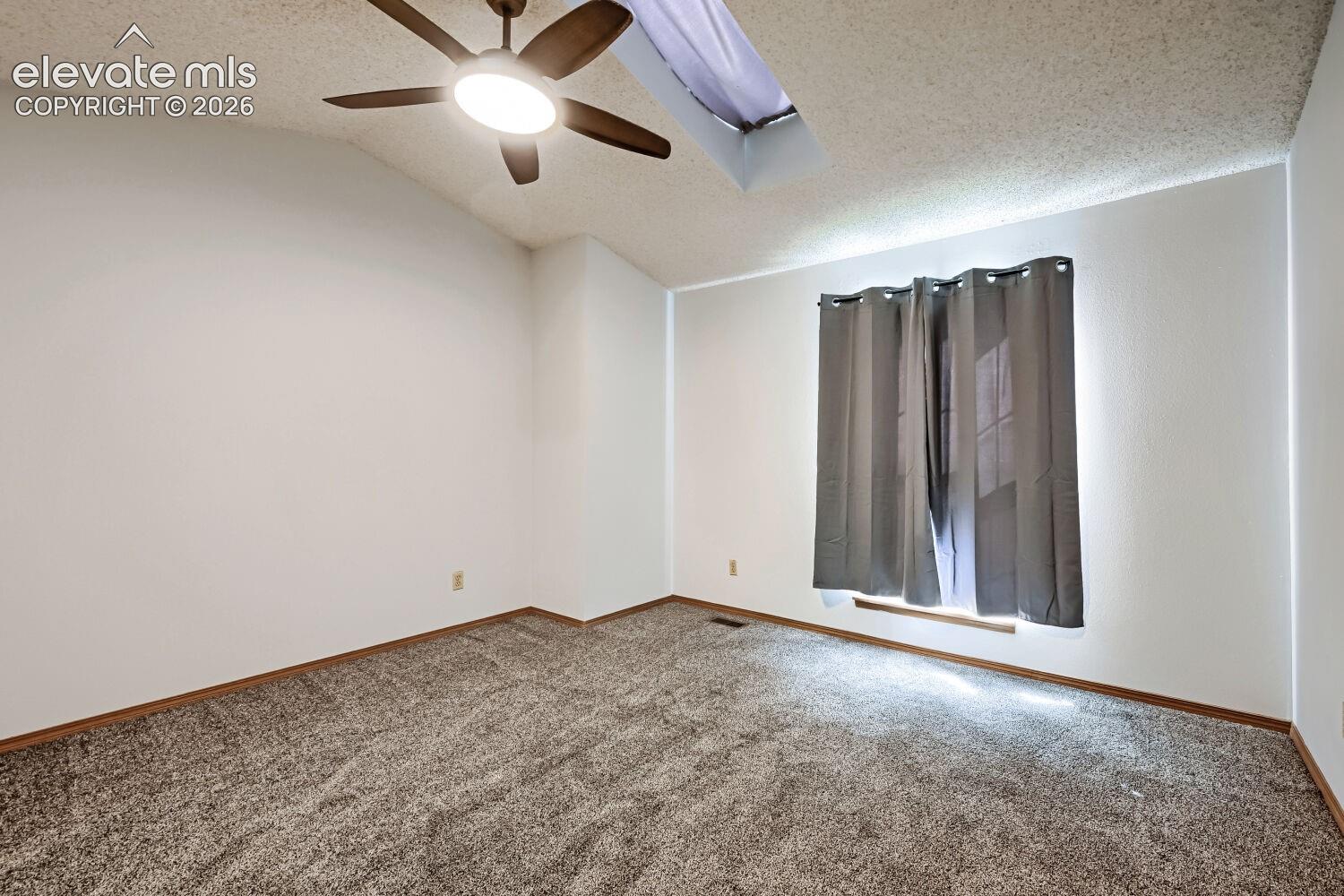 Vaulted ceiling with a ceiling fan, textured ceiling, window with curtain rod, and carpet flooring