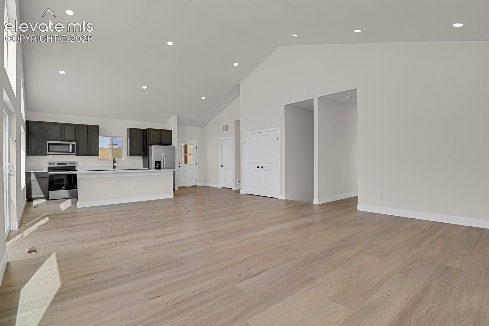 Open-concept interior featuring vaulted ceilings, recessed lighting, wood-finish flooring, and a kitchen with dark cabinetry and a peninsula