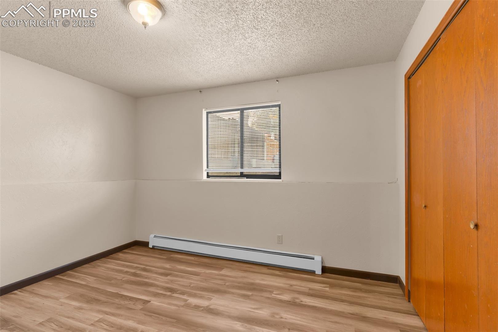 Unfurnished bedroom featuring baseboard heating, light wood finished floors, a closet, and a textured ceiling