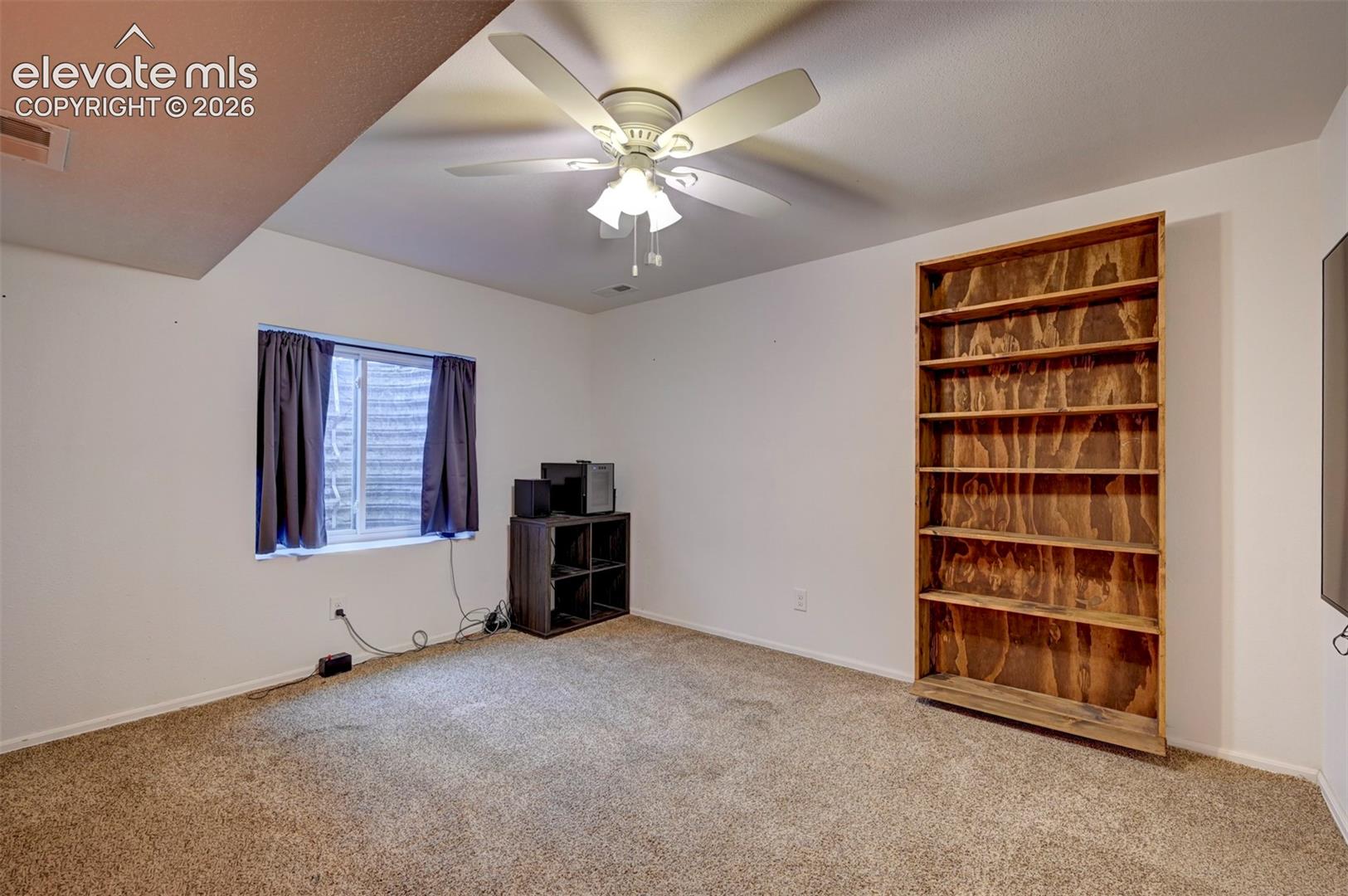 Built-in wood shelving, textured carpeting, and a ceiling fan with integrated lighting