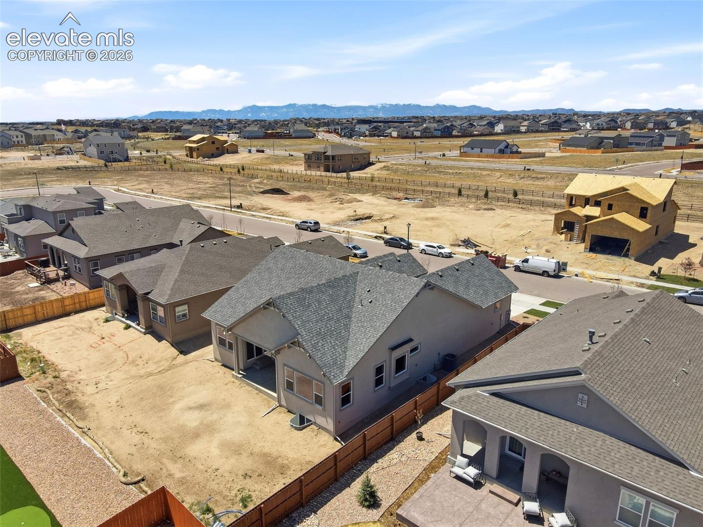 Aerial perspective featuring a residential neighborhood with mountain range backdrop, asphalt-shingled rooflines, and exterior wood fencing