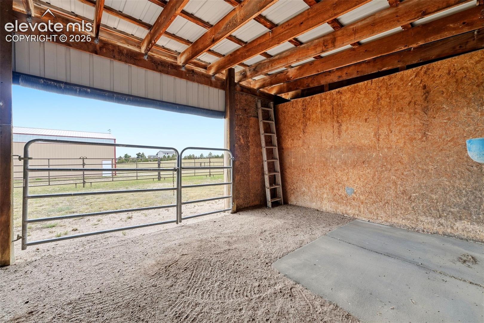Open-air structure with exposed wood beam ceiling, corrugated metal roofing, wood-panel walls, and a metal gate