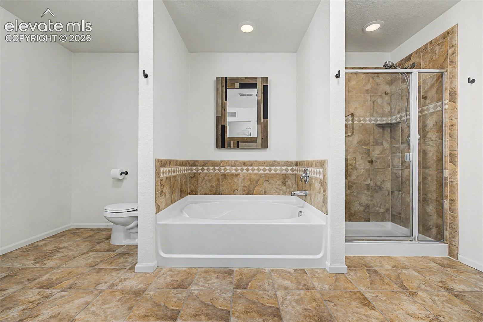 A deep soaking tub framed in warm stone tile sits beside a glass-enclosed shower, a primary bathroom that delivers a true spa experience without ever leaving home.