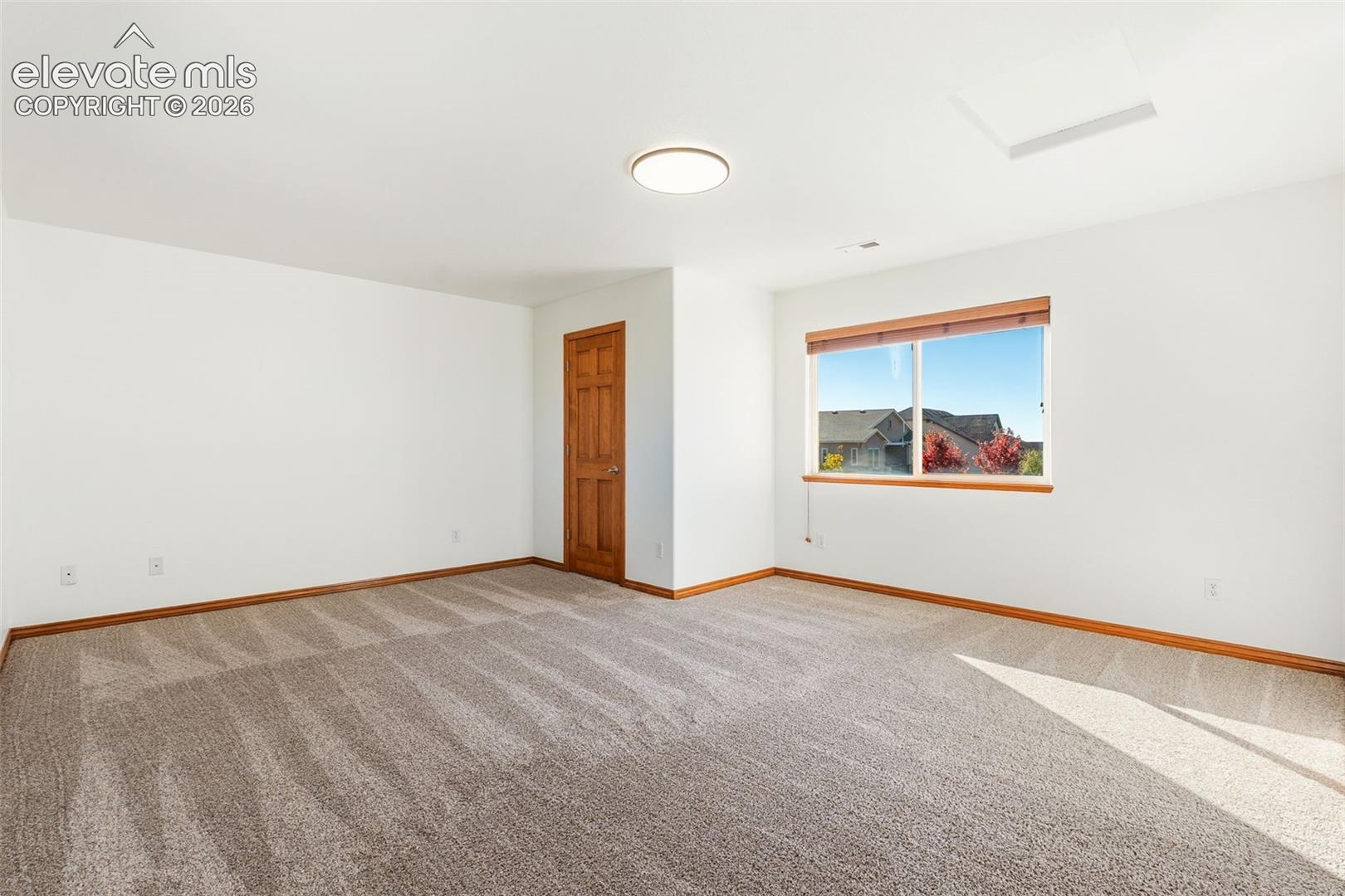 Neutral-toned wall-to-wall carpeting, wood-trimmed interior door, flush-mount lighting, and window featuring natural light