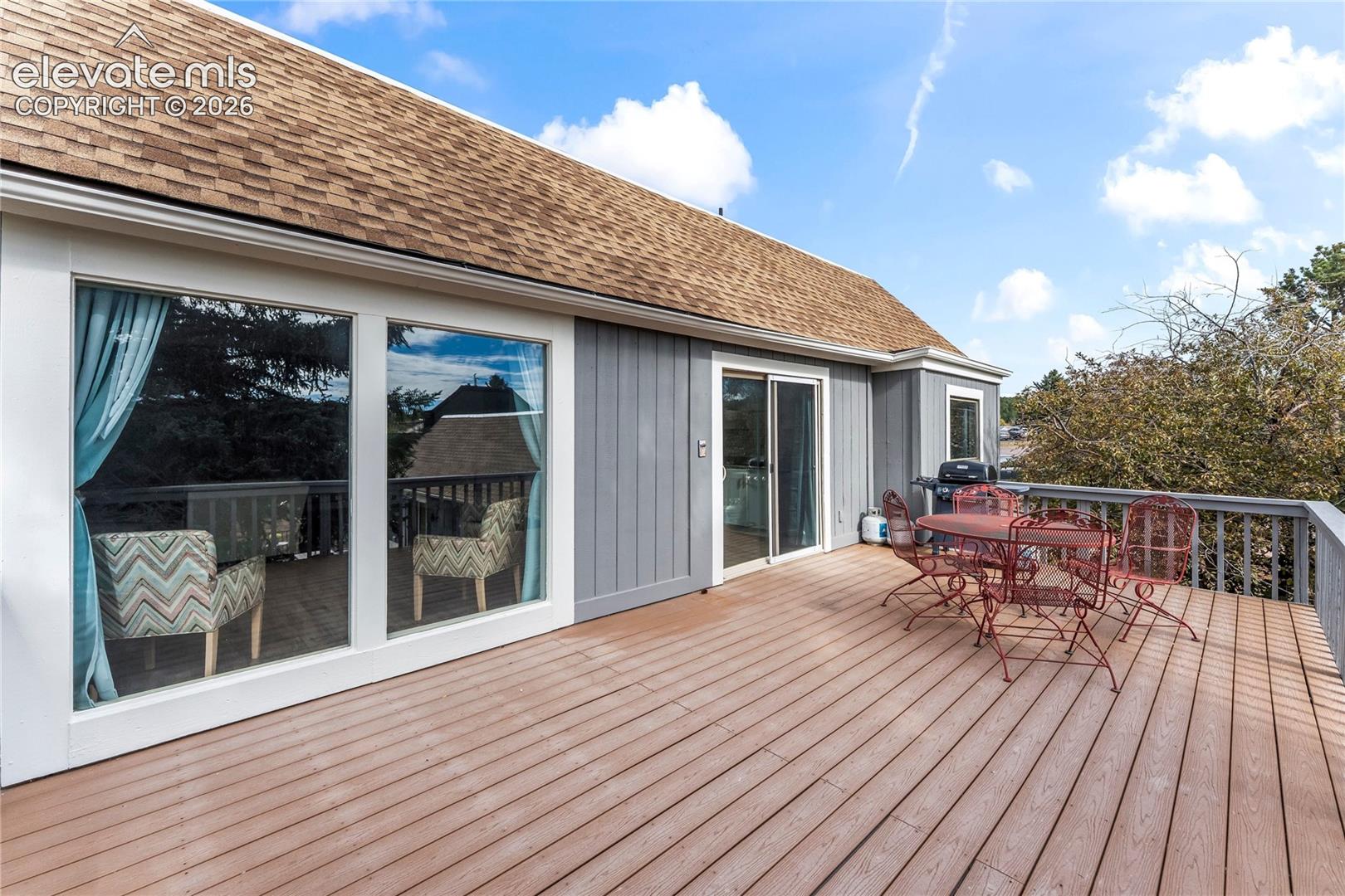 Expansive exterior wood-finish deck with vertical siding, shingle roofing, and glass sliding door access