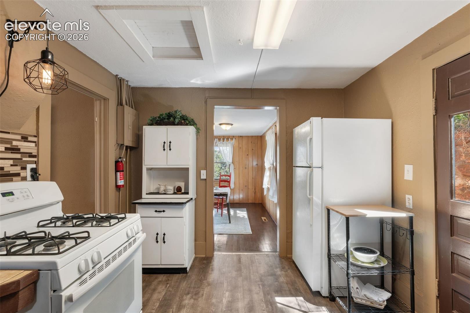 Kitchen space featuring wood-finish flooring, white cabinetry, a built-in oven range, and a white refrigerator