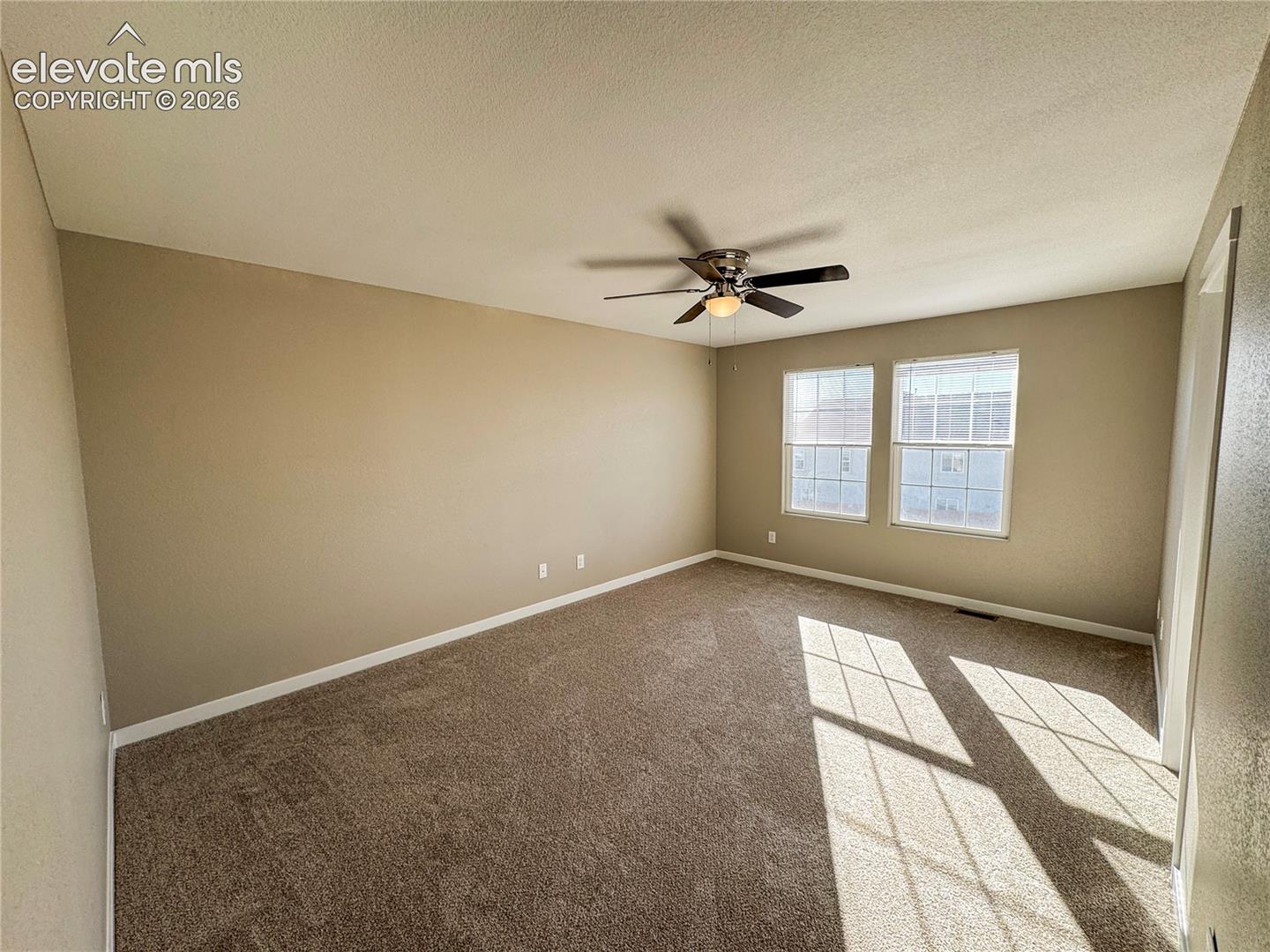 Interior space featuring neutral-toned walls, carpeting, dual windows, and a ceiling fan with integrated lighting