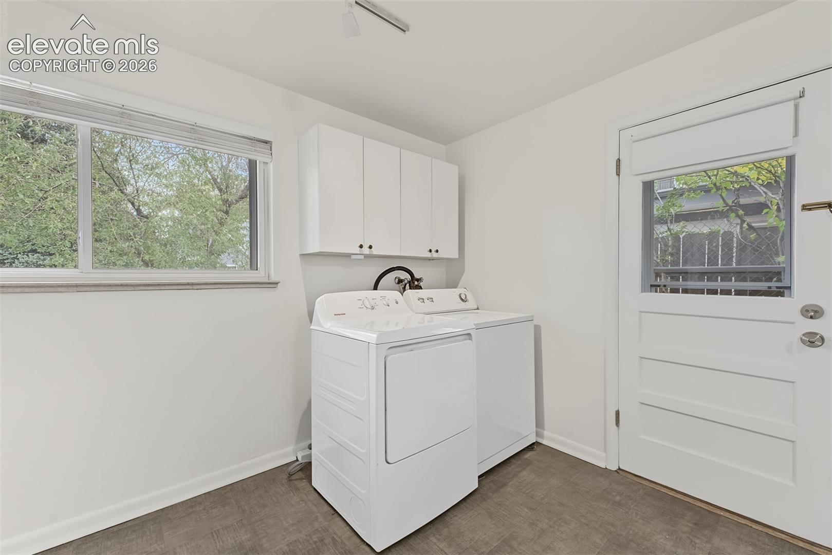 Laundry room featuring neutral vinyl flooring, white wall-mounted cabinetry, a large window, and an exterior door with a glass pane