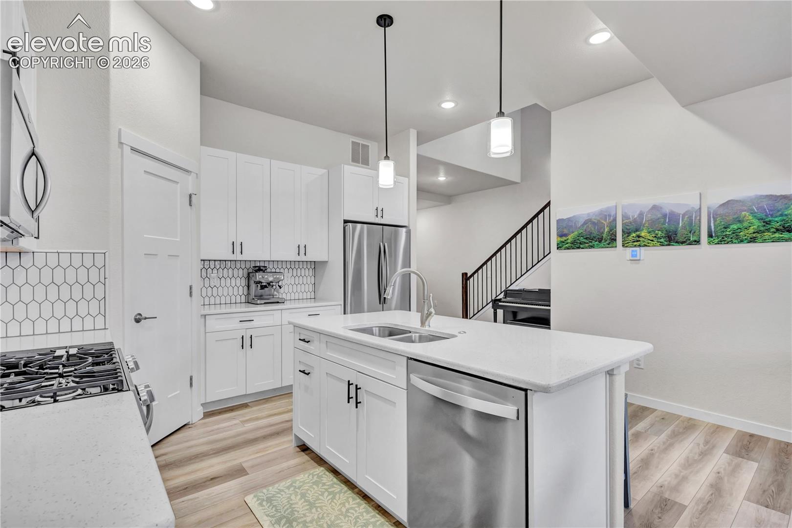 Modern kitchen featuring white cabinetry and countertops, stainless steel appliances, a kitchen island with an integrated sink, and wood-finish flooring