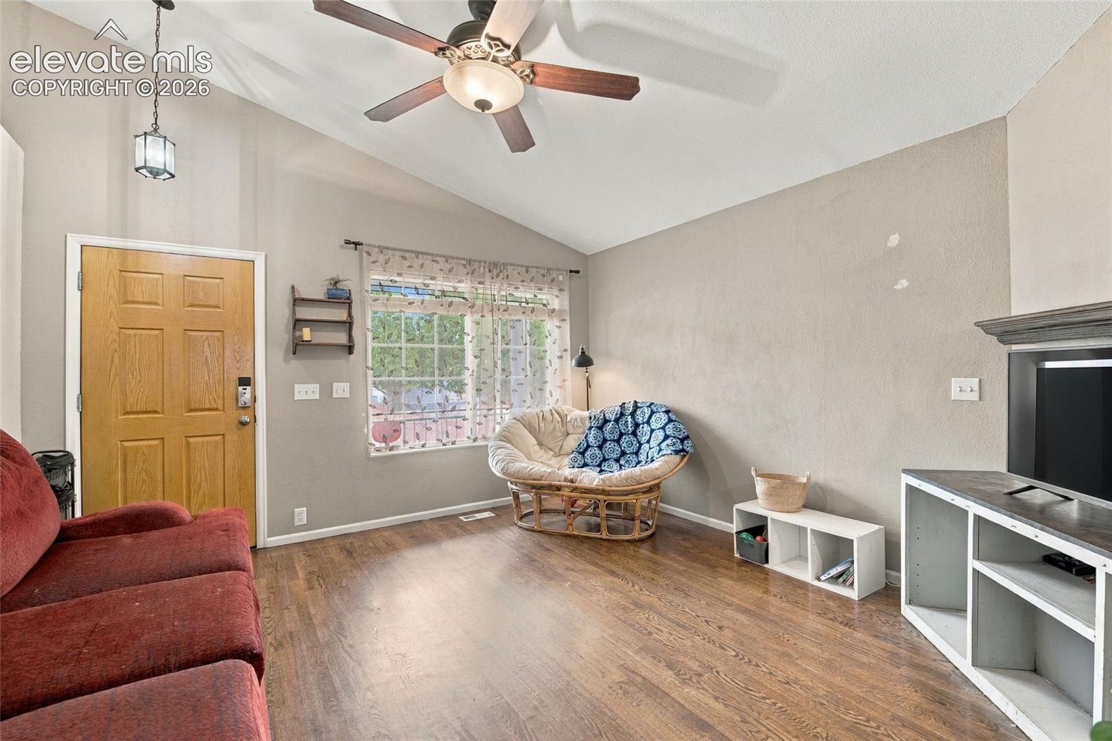 Living area featuring real wood flooring, a large window, and a built-in fireplace w/ mantle