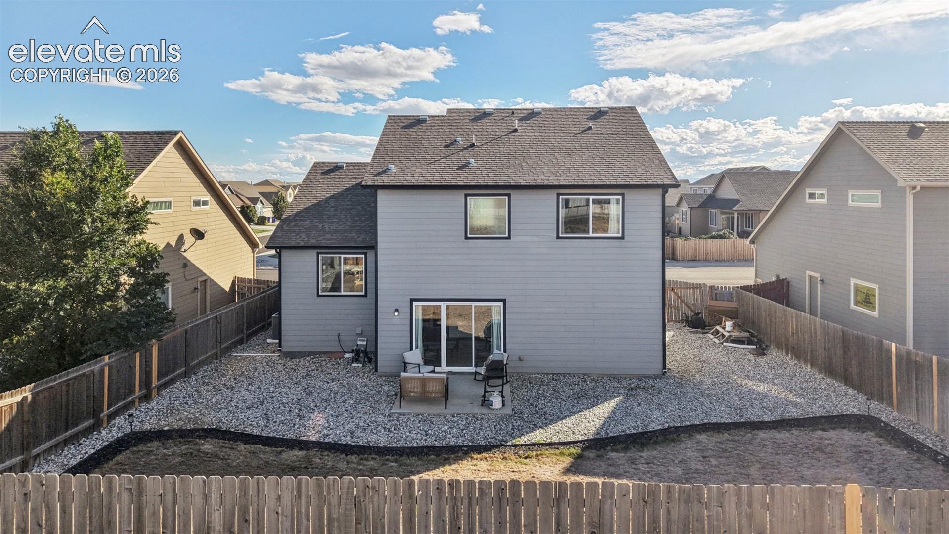 Rear exterior featuring horizontal lap siding, a composite shingle roof, a concrete patio, and a fenced backyard with decorative stone ground cover