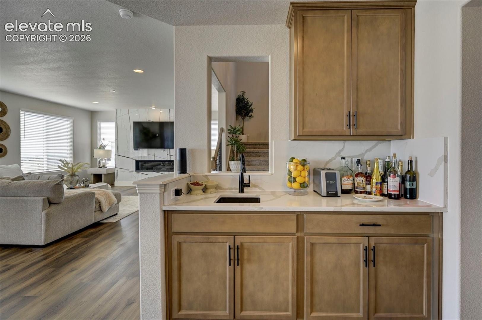 Built-in beverage station featuring light wood-finish cabinetry, a white countertop, and an undermount sink with a matte black faucet