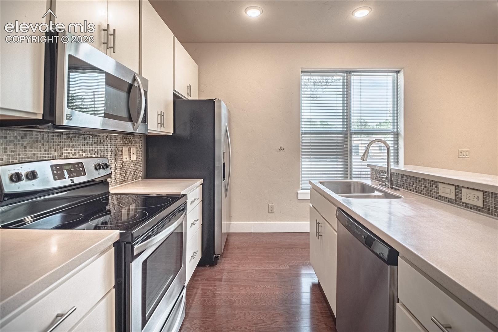 Contemporary kitchen featuring stainless steel appliances, mosaic tile backsplash, light-toned countertops, and wood-finish flooring