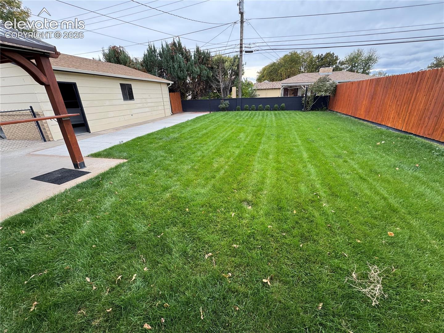 Backyard featuring a manicured lawn, concrete patio, detached garage structure, wood-tone privacy fencing, and a permanent timber-frame pavilion
