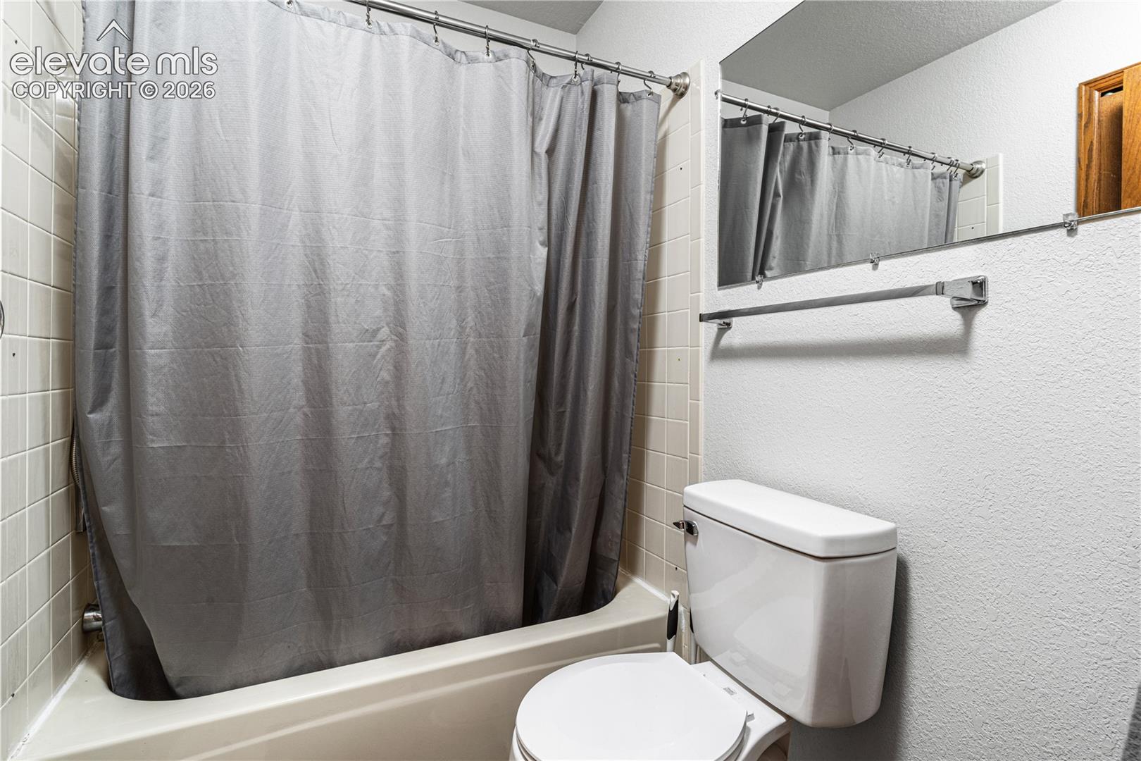 Full-height tiled shower surround, integrated acrylic tub, wall-mounted vanity mirror, and polished metal hardware