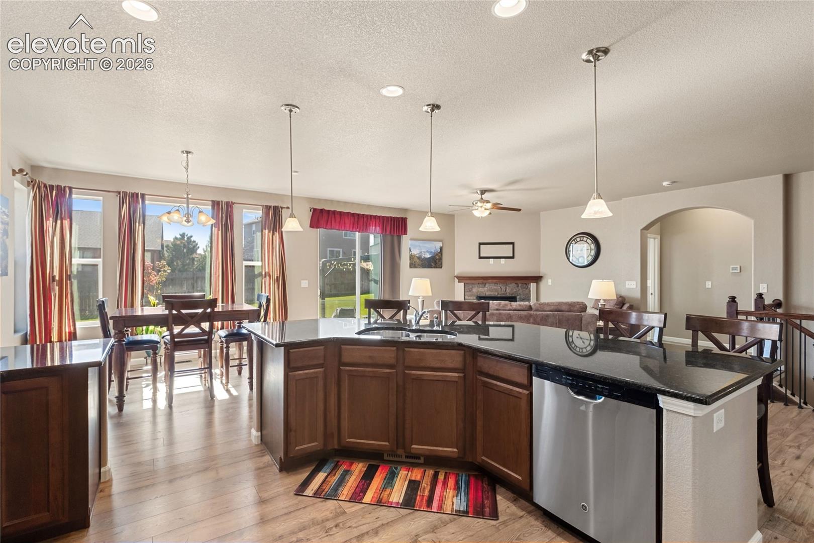 Kitchen featuring an expansive center island with stone-finish countertops, dark wood cabinetry, stainless steel dishwasher, pendant lighting, and wood-finish flooring