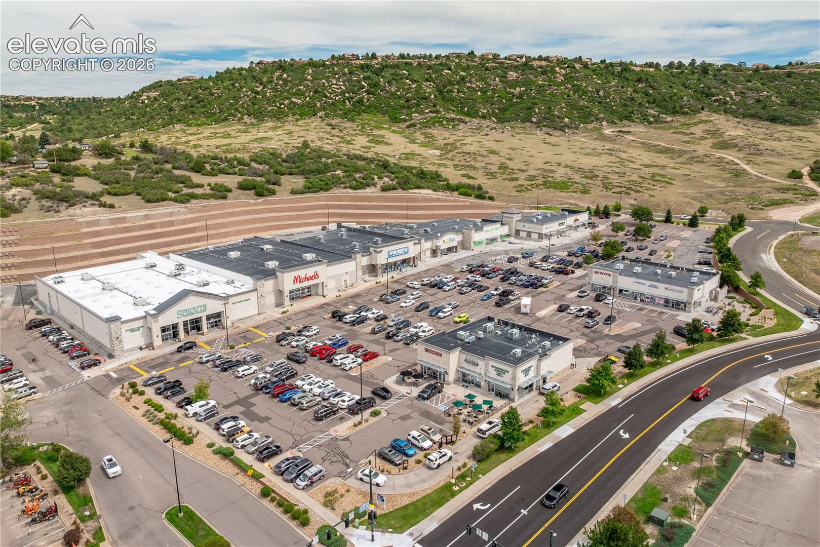 Commercial shopping center featuring multiple retail storefronts, expansive asphalt parking areas, and exterior building-mounted lighting