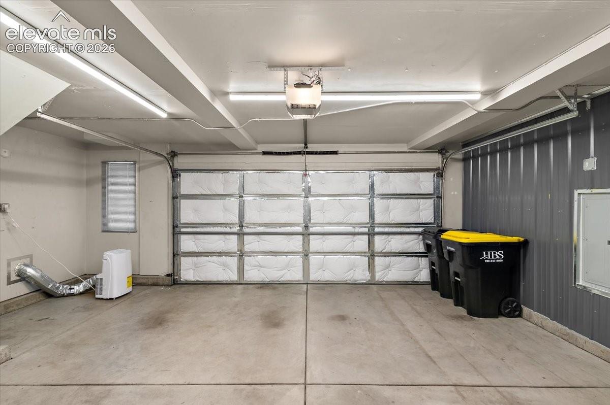 Concrete flooring, overhead strip lighting, insulated garage door, corrugated metal wall paneling, and a small window with blinds