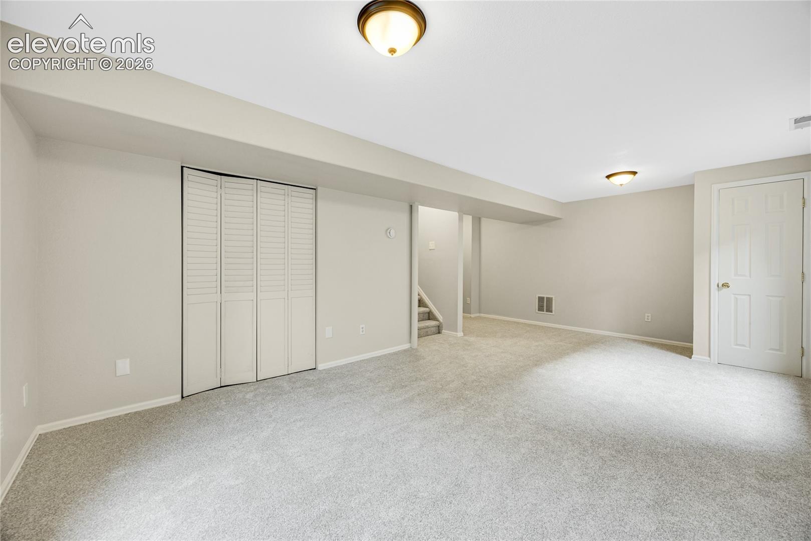 Neutral-toned interior featuring wall-to-wall carpeting, white bi-fold closet doors, flush-mount ceiling lighting, and a solid-core interior door