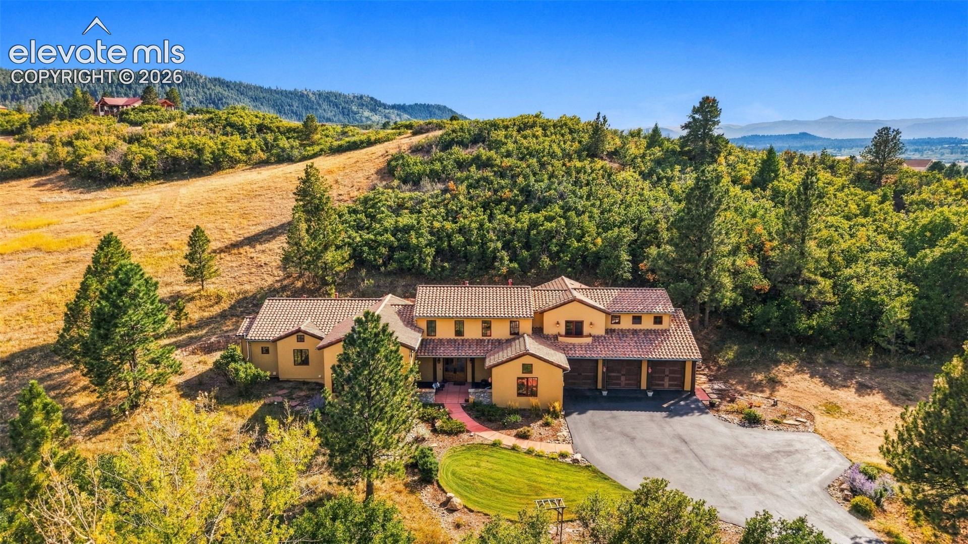 Multi-level stucco exterior with a tiled roof, integrated garage, and a winding asphalt driveway