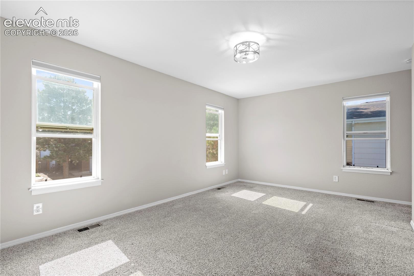 Room featuring neutral wall paint, carpeted flooring, three double-hung windows, and a flush-mount geometric ceiling light fixture