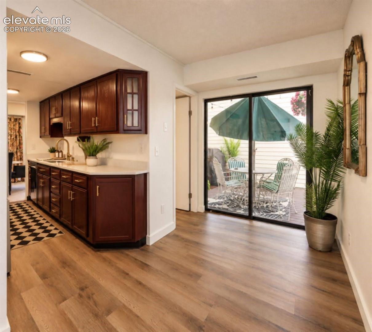 Kitchen featuring rich-toned cabinetry with glass-panel accents, stone-surface countertops, brushed gold-finish hardware, wood-finish flooring, and a large sliding glass door