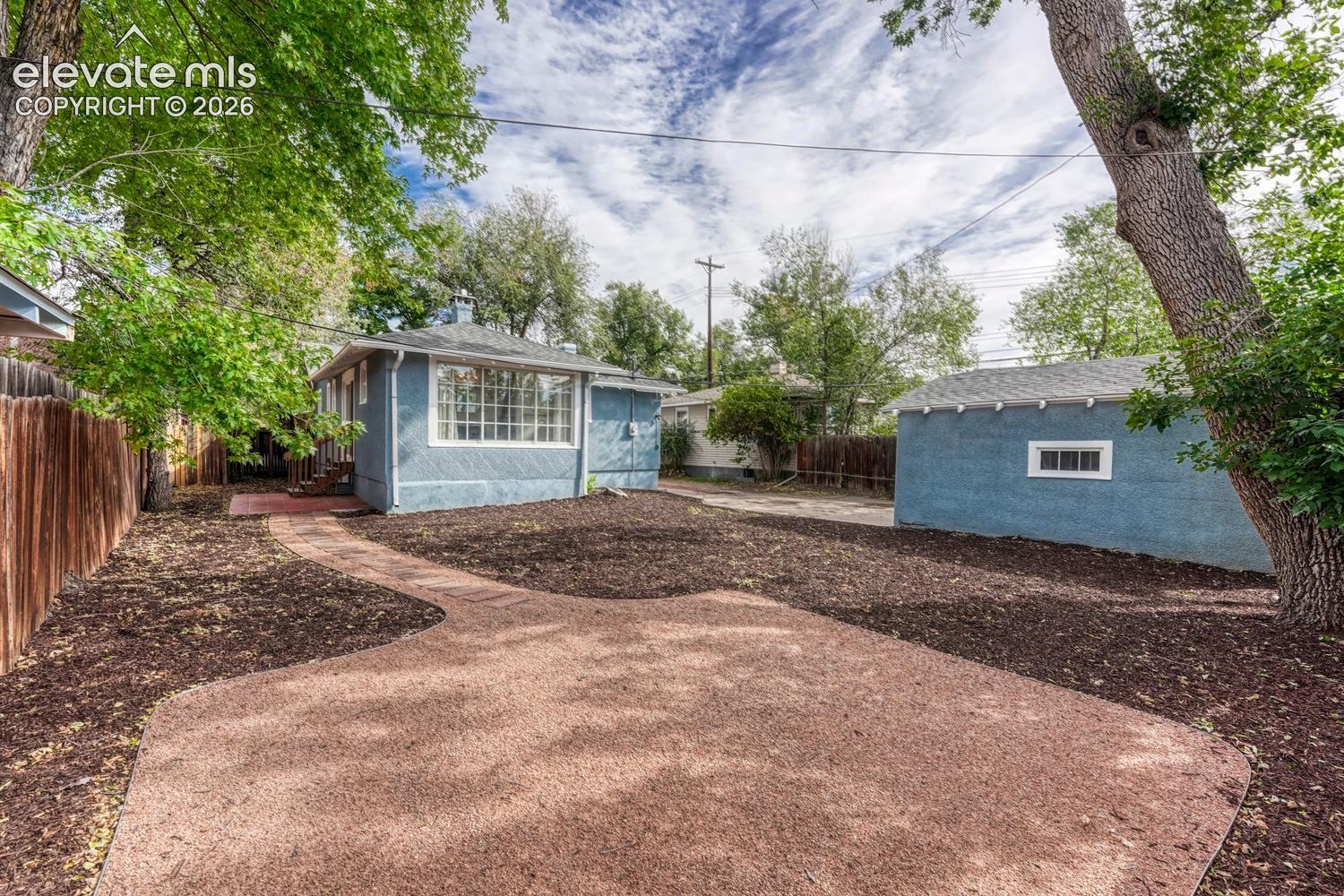 Private backyard with a detached garage, mature trees, and a curved paved pathway