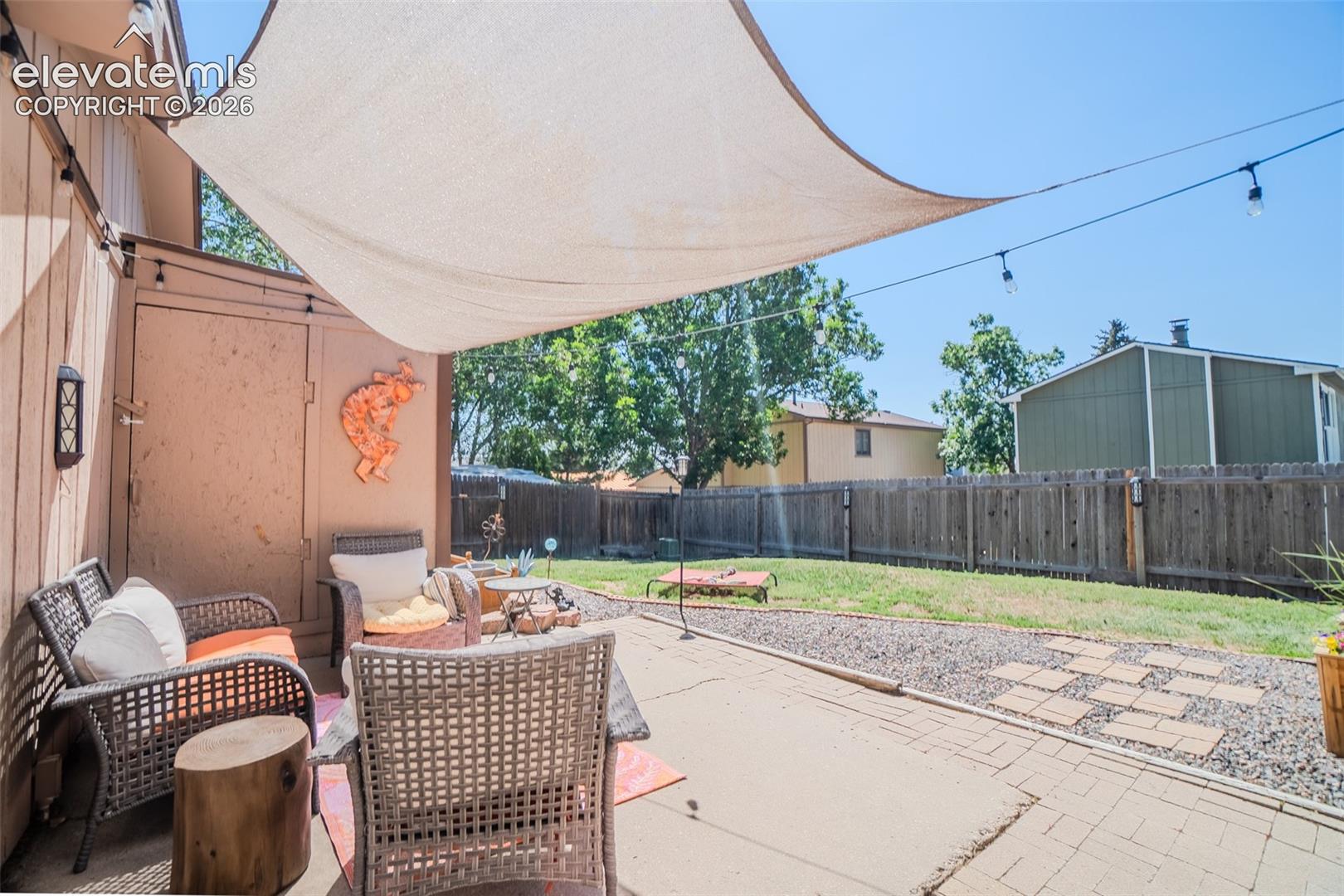 Patio area featuring a neutral-toned sunshade, string lighting, and a paved surface